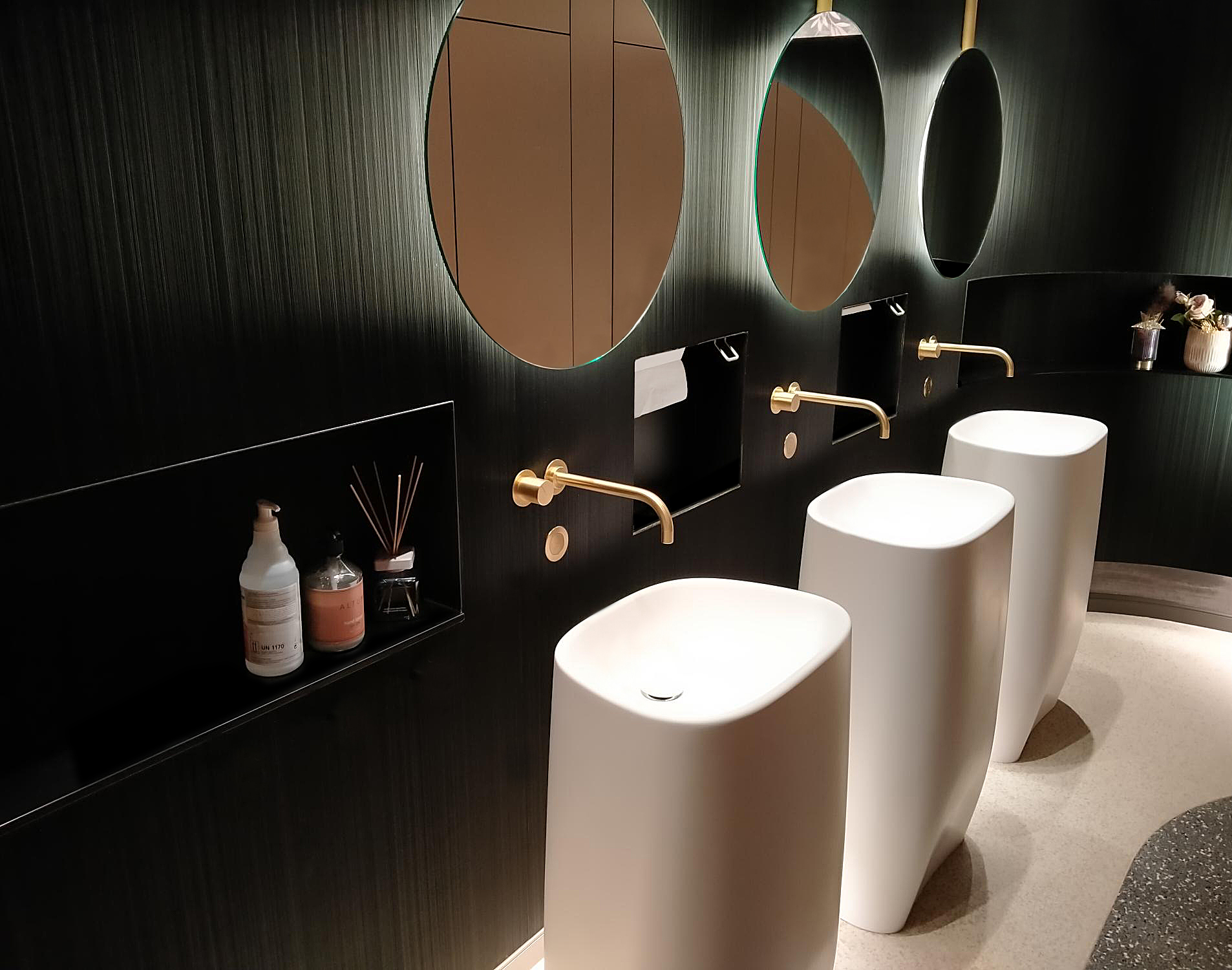 Drie witte wastafels met gouden kranen, spiegels en ingebouwde dispensers